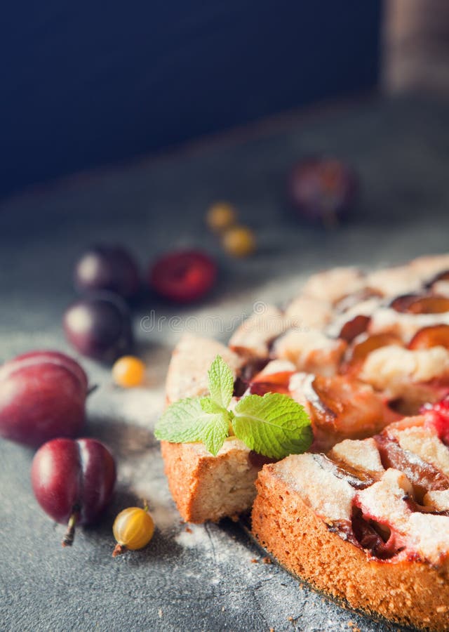 Homemade summer plum cake garnished with gooseberry and mint on dark background. Homemade summer plum cake garnished with gooseberry and mint on dark background