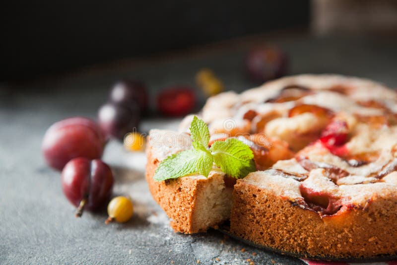 Homemade summer plum cake garnished with gooseberry and mint on dark background. Homemade summer plum cake garnished with gooseberry and mint on dark background