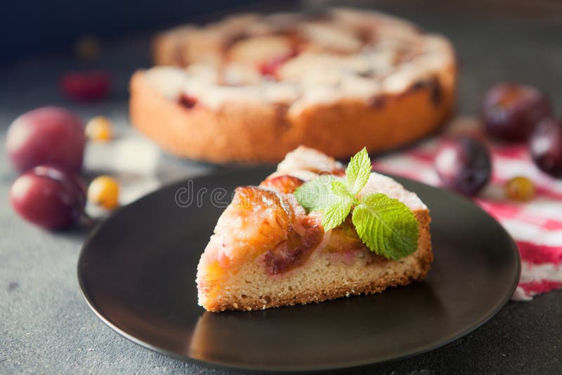 Homemade summer plum cake garnished with gooseberry and mint on dark background. Homemade summer plum cake garnished with gooseberry and mint on dark background