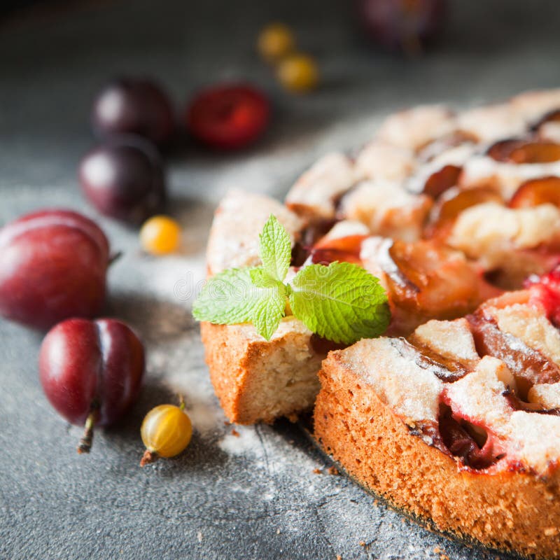 Homemade summer plum cake garnished with gooseberry and mint on dark background. Homemade summer plum cake garnished with gooseberry and mint on dark background