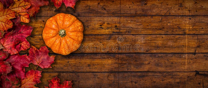 A rustic wooden background with autumn foliage and a pumpkin