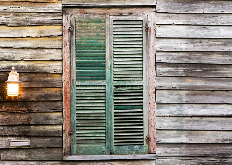 Rustic wooden building window with closed green shutters and light