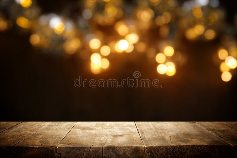 Rustic wooden table in front of glitter black and gold bokeh lights.