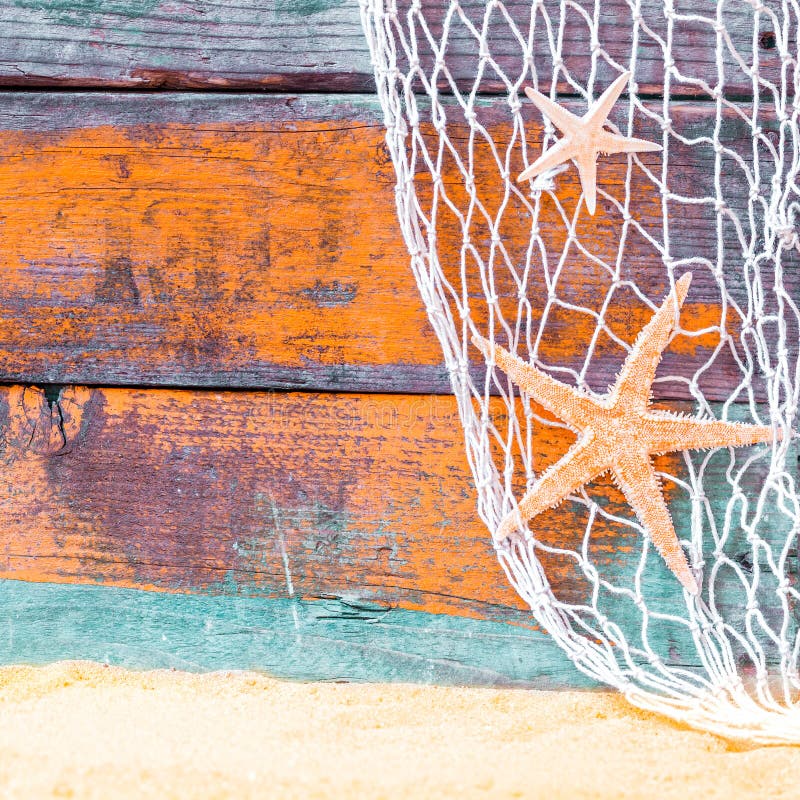 Rustic nautical background with starfish hanging in a fishing net against weathered painted wooden boards in blue and orange with copyspace over golden tropical beach sand. Rustic nautical background with starfish hanging in a fishing net against weathered painted wooden boards in blue and orange with copyspace over golden tropical beach sand
