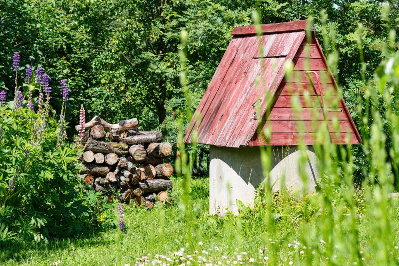 Rustikales hölzernes Wasser gut mit Woodpile des Brennholzes lizenzfreie stockfotografie Rustikales hölzernes Wasser gut mit Woodpile des Brennholzes lizenzfreie stockfotografie
