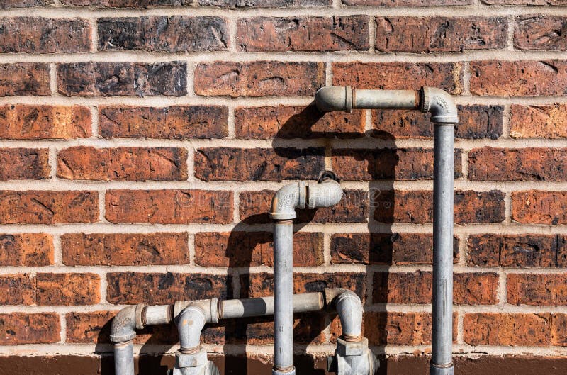 Rusty iron water pipeline on exterior brown brick wall.