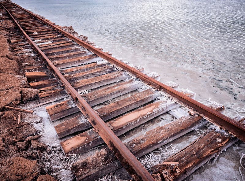 Rusty razy rails and rotten sleepers covered of salt on old railroad tracks on a mound at salt mining lake near brine stock photos Rusty razy rails and rotten sleepers covered of salt on old railroad tracks on a mound at salt mining lake near brine stock photos