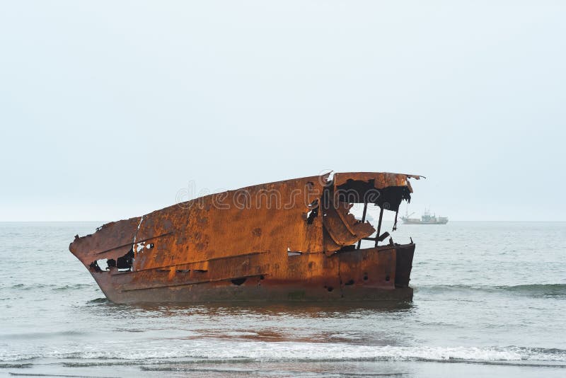 Rusty shipwreck against a foggy seascape with a sailing ship stock photography