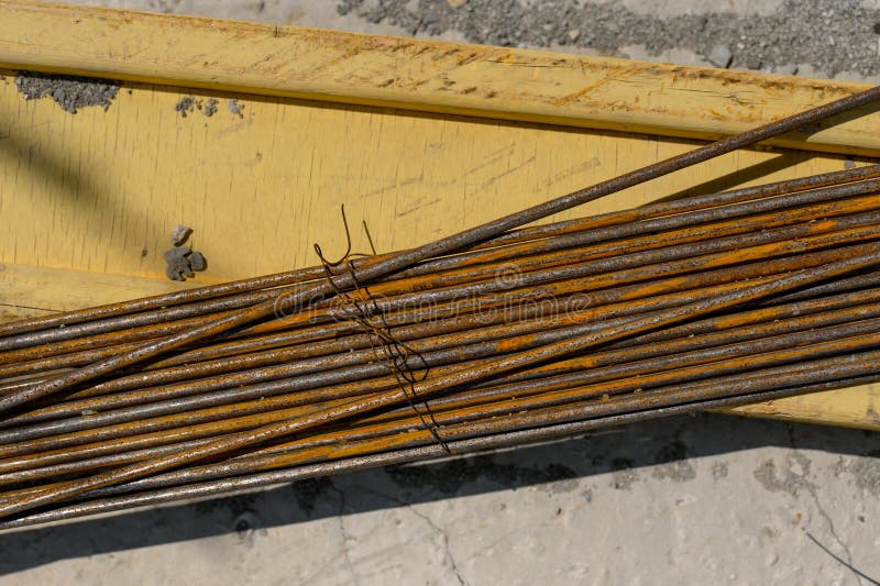 Rusty steel rebar is stacked on a yellow construction material, with a concrete surface visible underneath, illuminated by bright sunlight. Load structural stock images, royalty-free photos and pictures