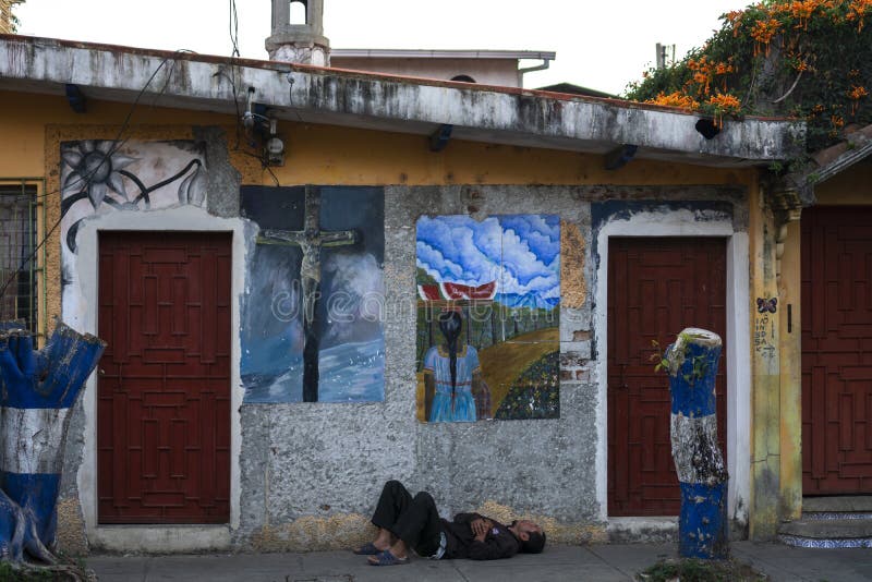 Ruta de las Flores, El Salvador - January 29, 2022: Homeless man sleeping at the door of building with murals in El Salvador. Ruta de las Flores, El Salvador - January 29, 2022: Homeless man sleeping at the door of building with murals in El Salvador.