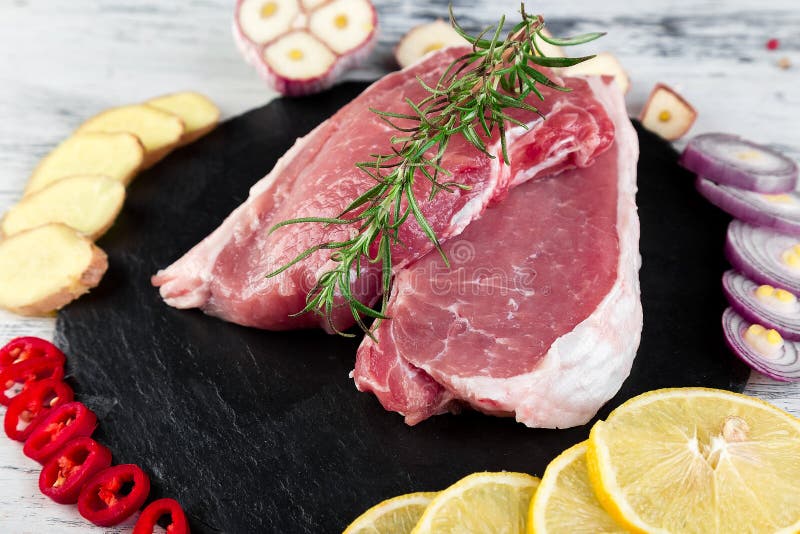 Ruw varkensvleesvlees op zwarte leiplaat met kruidingrediënt royalty-vrije stock afbeeldingen Ruw varkensvleesvlees op zwarte leiplaat met kruidingrediënt royalty-vrije stock afbeeldingen
