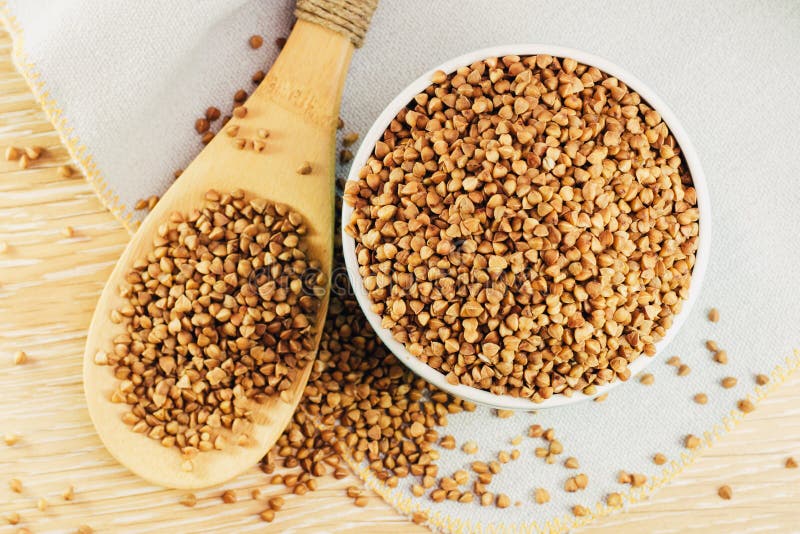 Ruwe boekweitkorrels in een kom en in een houten lepel op de lijst stock afbeeldingen Ruwe boekweitkorrels in een kom en in een houten lepel op de lijst stock afbeeldingen