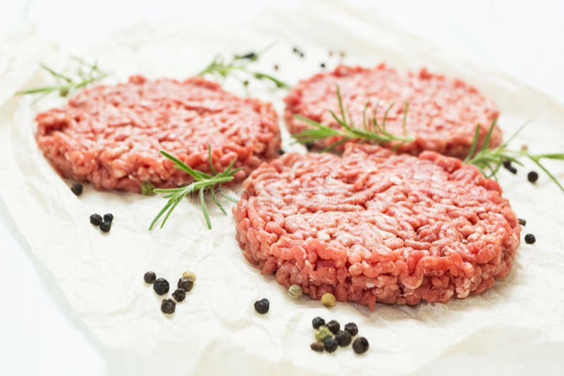 Ruwe hamburgers zonder vet van organisch rundvlees op een witte houten achtergrond met kruiden Hoog - kwaliteitsgehakt stock afbeelding Ruwe hamburgers zonder vet van organisch rundvlees op een witte houten achtergrond met kruiden Hoog - kwaliteitsgehakt stock afbeelding