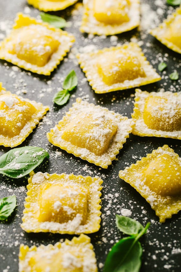 Tasty raw ravioli with flour and basil on dark background. Process of making italian ravioli. Closeup. Tasty raw ravioli with flour and basil on dark background. Process of making italian ravioli. Closeup