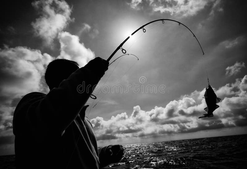 Black and white image of a sea fisherman having caught a fish, the sun behind his fishing rod. Black and white image of a sea fisherman having caught a fish, the sun behind his fishing rod.