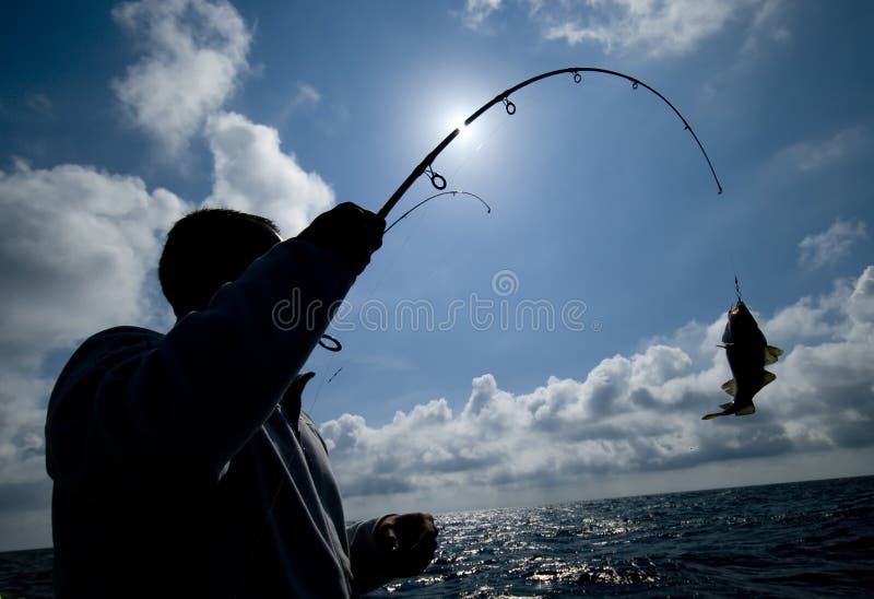 A sea fisherman silhouette, he caught a fish, the sun behind his bent fishing rod. A sea fisherman silhouette, he caught a fish, the sun behind his bent fishing rod.