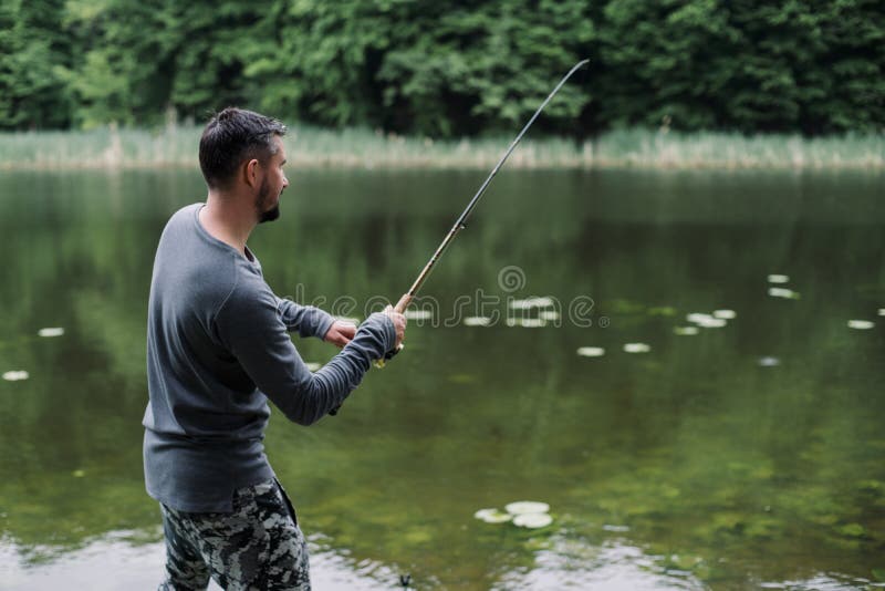 Fisherman cast fishing rod in lake or river water. Man with spinning tackle in green forest. Adventure, sport, activity. Spin fishing, angling, catching. Healthy lifestyle. Fisherman cast fishing rod in lake or river water. Man with spinning tackle in green forest. Adventure, sport, activity. Spin fishing, angling, catching. Healthy lifestyle.