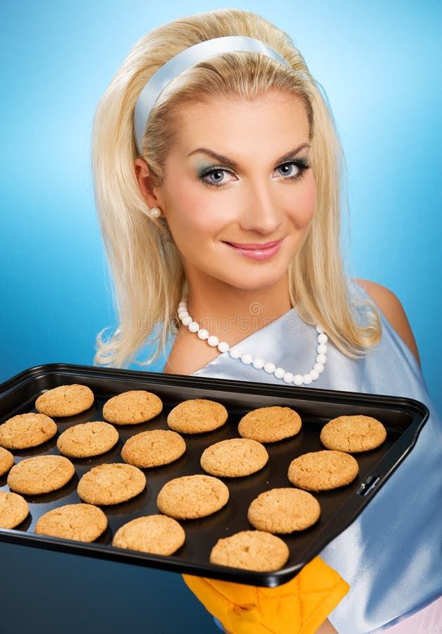 Beautiful woman holding hot roasting pan with oat cookies on it. Retro stylized portrait. Beautiful woman holding hot roasting pan with oat cookies on it. Retro stylized portrait