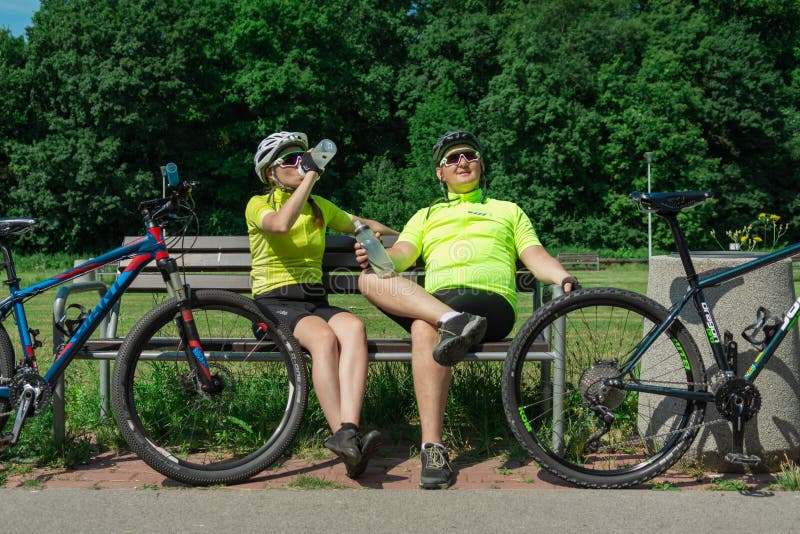 Rzeszow, Poland - Jun 23.2019 A young guy and a young girl are resting after a bike ride, drinking water, sitting on a bench.