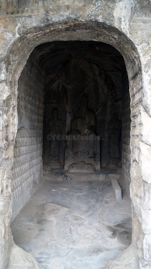 Buddha sculpture in a niche, Longmen grottoes with several niches carved in the wall at the face of a mountain, buddhist temple whit several sculptures in it and a fence in front of it. Buddha sculpture in a niche, Longmen grottoes with several niches carved in the wall at the face of a mountain, buddhist temple whit several sculptures in it and a fence in front of it