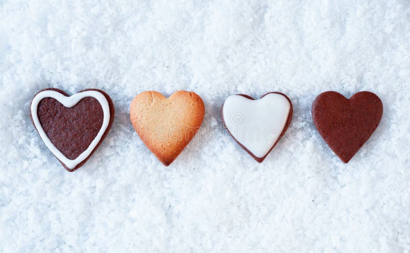 Row of crisp baked gingerbread hearts on a snowy background with copyspace above and below for Christmas greetings. Row of crisp baked gingerbread hearts on a snowy background with copyspace above and below for Christmas greetings