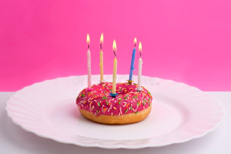 Różowy pączek na bielu talerzu jak urodzinowy tort z świeczkami na bielu i menchii tle zdjęcia royalty free Różowy pączek na bielu talerzu jak urodzinowy tort z świeczkami na bielu i menchii tle zdjęcia royalty free