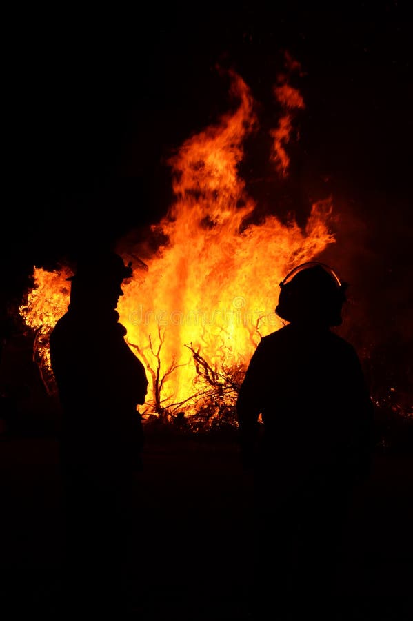 A unique image showing silhouettes of two brave firemen on duty standing in front looking at the oncoming bushfire. The photograph shows the red hot centre or eye of the fire which is not easily captured. A unique image showing silhouettes of two brave firemen on duty standing in front looking at the oncoming bushfire. The photograph shows the red hot centre or eye of the fire which is not easily captured.