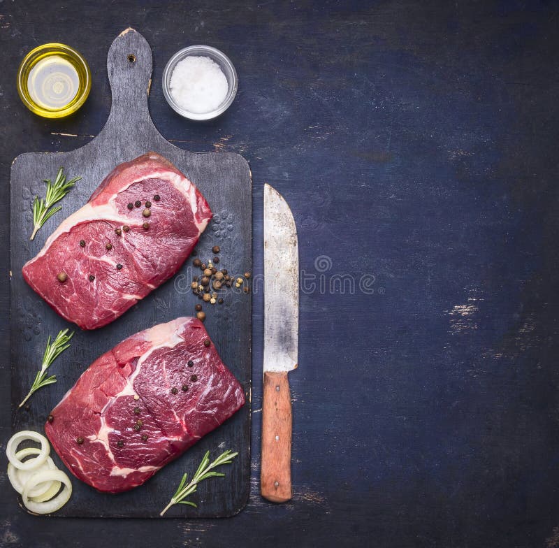 Rå nötköttbiff med rosmarin, olja och kött dela sig på den mörka lantliga skärbrädan, bästa sikt med utrymme för text royaltyfria foton Rå nötköttbiff med rosmarin, olja och kött dela sig på den mörka lantliga skärbrädan, bästa sikt med utrymme för text royaltyfria foton