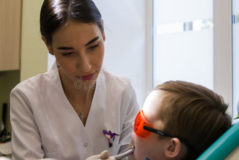Réception à l'art dentaire Un jeune dentiste féminin examine la cavité buccale d'un enfant photo stock Réception à l'art dentaire Un jeune dentiste féminin examine la cavité buccale d'un enfant photo stock