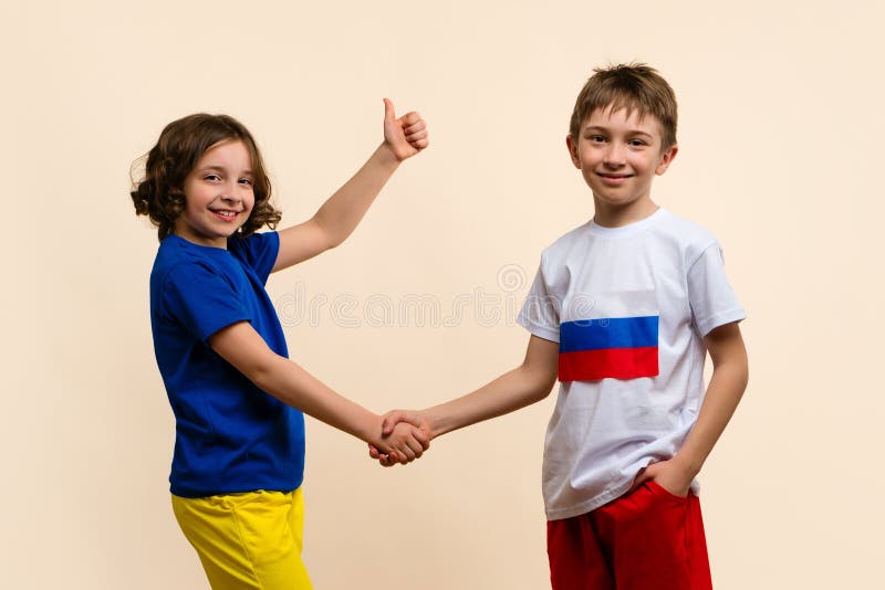 Children Girl and Boy in outfits in colors flags of Russia and Ukraine shake hands. Child shows thumb up sign ok. Concept Successful truce negotiations. Reconciliation. Friendship fraternal peoples. Children Girl and Boy in outfits in colors flags of Russia and Ukraine shake hands. Child shows thumb up sign ok. Concept Successful truce negotiations. Reconciliation. Friendship fraternal peoples
