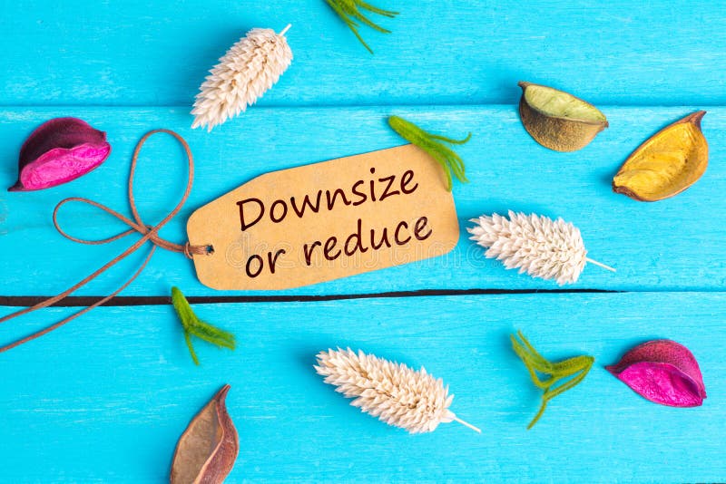 Downsize or reduce text on paper tag with rope and color dried flowers around on blue wooden background. Downsize or reduce text on paper tag with rope and color dried flowers around on blue wooden background