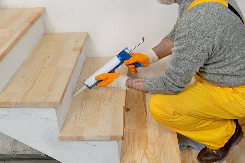 Rénovation à la maison, calfeutrant les escaliers en bois avec du silicone image stock Rénovation à la maison, calfeutrant les escaliers en bois avec du silicone image stock