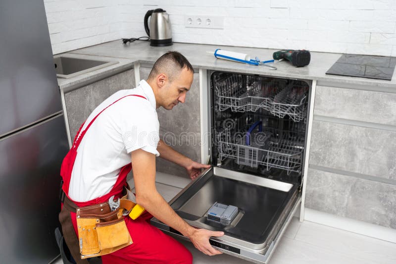 Réparateur Jeune Travailleur De Service Réparation De Lave-Vaisselle Appliance Dans Cuisine photographie stock libre de droits