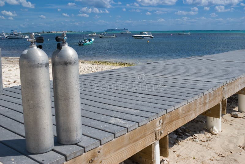 Scuba Tanks on dock ready for divers in Grand Cayman. Dive boats in Background. Scuba Tanks on dock ready for divers in Grand Cayman. Dive boats in Background.