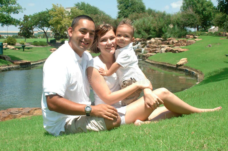 Young married couple with their toddler child. New family taking pictures in white shirts and tan shorts. Family of three. Young married couple with their toddler child. New family taking pictures in white shirts and tan shorts. Family of three.