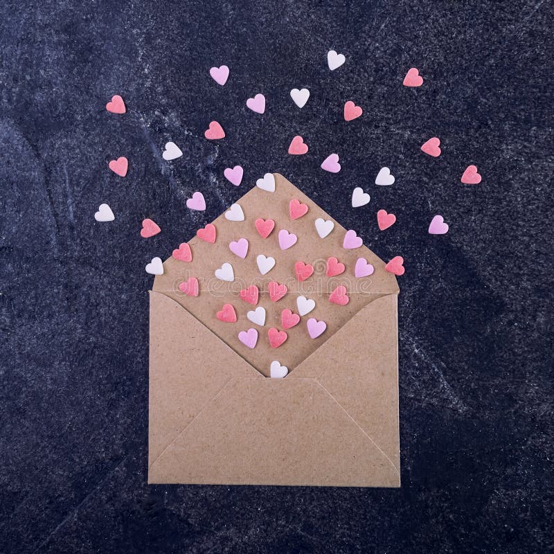 Röda och vita för sötsaksockergodisen hjärtor för rosa färger, flyger ut ur hantverkpapperskuvert på den mörka stenbakgrunden iso arkivbild Röda och vita för sötsaksockergodisen hjärtor för rosa färger, flyger ut ur hantverkpapperskuvert på den mörka stenbakgrunden iso arkivbild