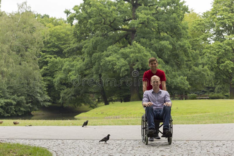 Disabled men on wheelchair during a stroll in the park with his smiling friend. Disabled men on wheelchair during a stroll in the park with his smiling friend