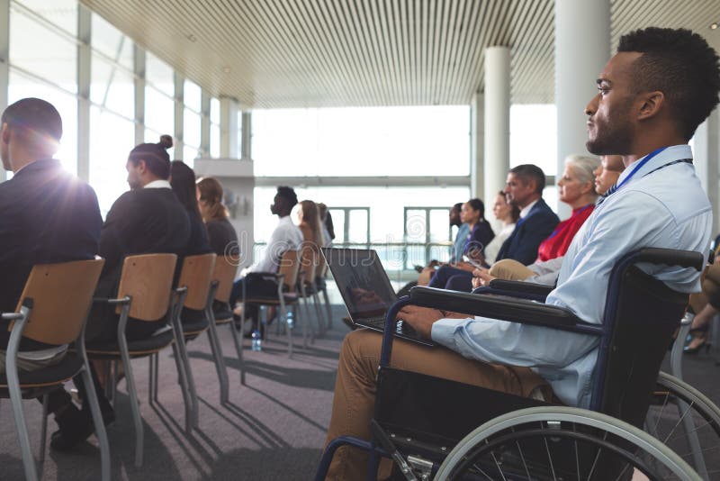 Rörelsehindrad ung affärsman som använder bärbara datorn under seminarium royaltyfri fotografi Rörelsehindrad ung affärsman som använder bärbara datorn under seminarium royaltyfri fotografi