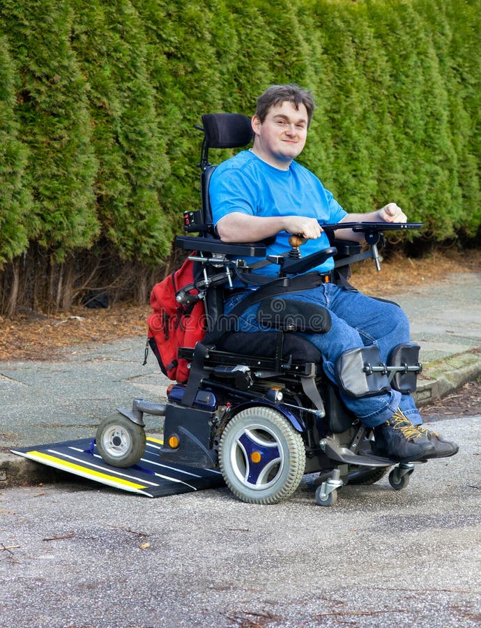 Mobility for infantile cerebral palsy patients caused by birth complications with a spastic young man in a multifunctional wheelchair negotiating a mobile ramp on a kerb during an integration Outing. Mobility for infantile cerebral palsy patients caused by birth complications with a spastic young man in a multifunctional wheelchair negotiating a mobile ramp on a kerb during an integration Outing.