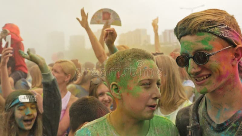 RÚSSIA, IRKUTSK - 27 DE JUNHO DE 2018: Jovens felizes que dançam e que comemoram durante o festival de Holi das cores Multidão de