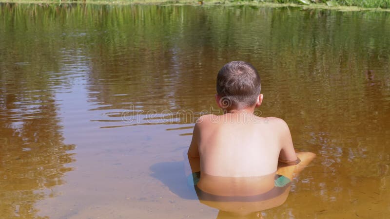 Rückansicht eines Kindes auf Sand bis zur Taille in einem transparenten flachen Fluss