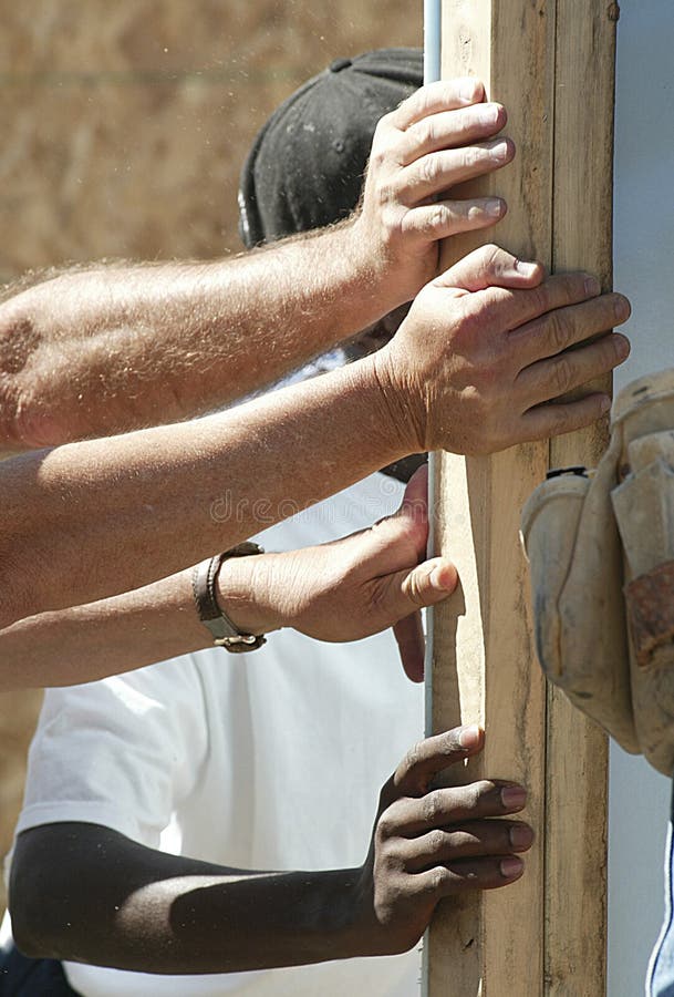 Volunteers helping with house construction- hands supporting the wall of the house. Volunteers helping with house construction- hands supporting the wall of the house