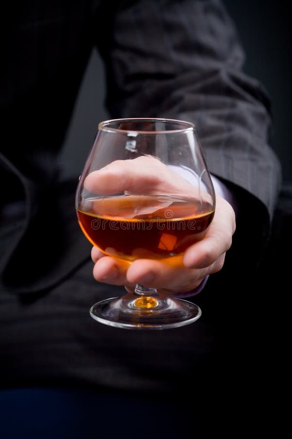 Hand with glass of cognac over black background. Focus on hand with glass. Hand with glass of cognac over black background. Focus on hand with glass.