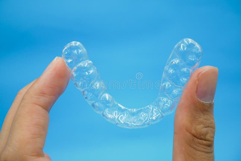 Ręka trzymająca przezroczyste plastikowe zęby na tle niebieskiego nieba to sprzęt dla ortodontów.