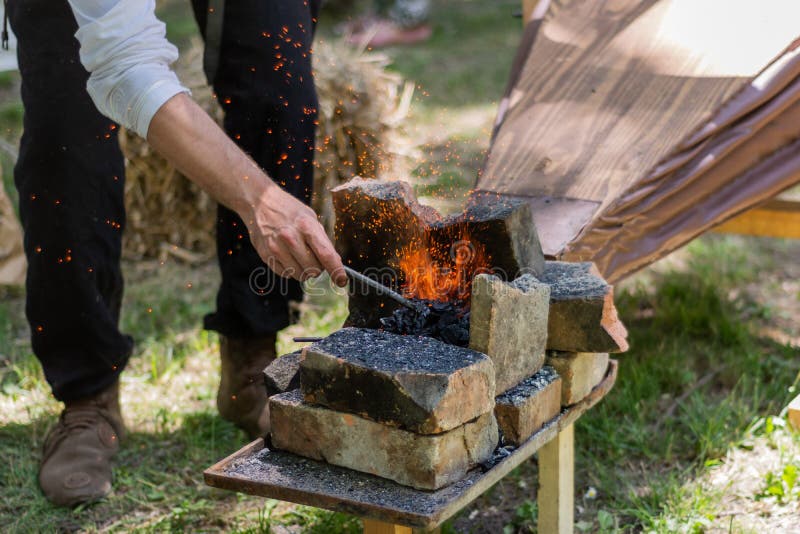 Ręka z kawałkiem ogrzewającym w węglowym ogieniu żelazo i bellows robimy iskrom od blacksmith narzędzi obraz stock Ręka z kawałkiem ogrzewającym w węglowym ogieniu żelazo i bellows robimy iskrom od blacksmith narzędzi obraz stock