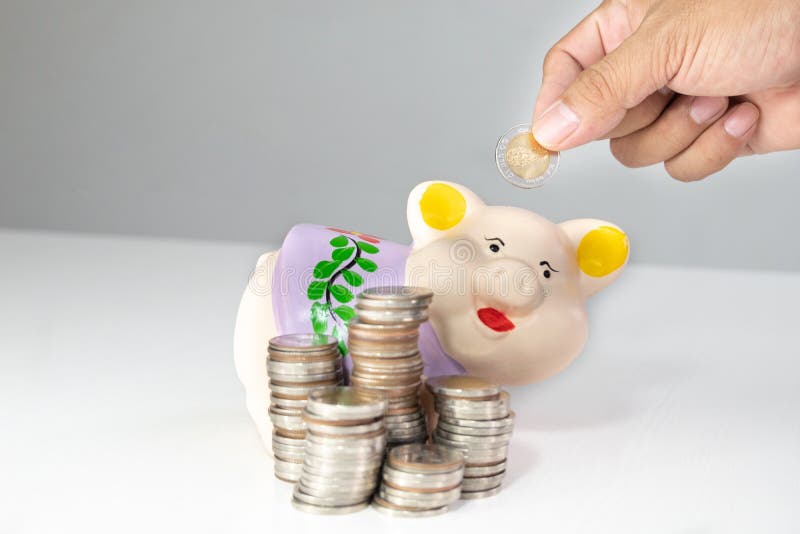 Ręki kładzenia moneta w Purpurowego prosiątko banka z monetami wypiętrza zdjęcia stock Ręki kładzenia moneta w Purpurowego prosiątko banka z monetami wypiętrza zdjęcia stock