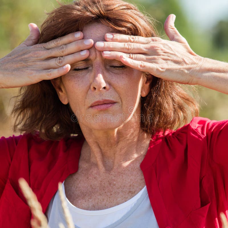 50s brunette woman massaging forehead to soothe sinus pain outdoors