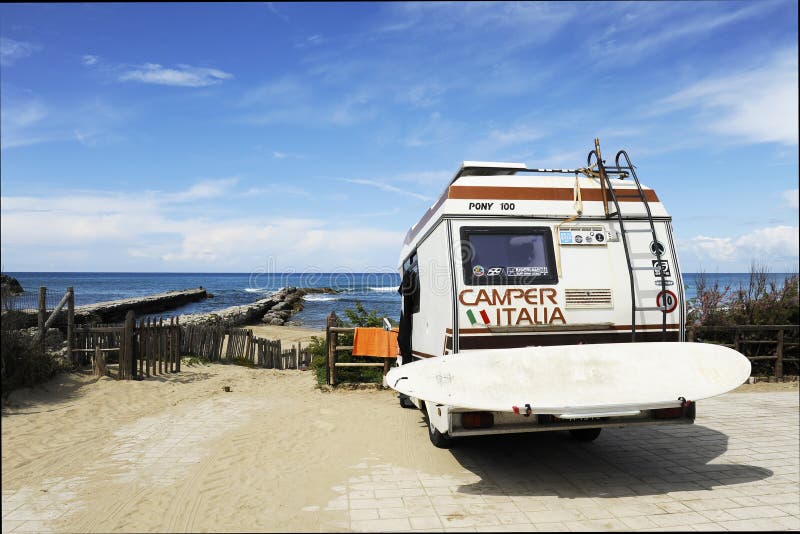 Sabaudia, Lazio, Italien - 12. April 2018: Rückseite des Weinlesecampers geparkt auf der Strandküste mit einem Surfbrett auf zurü lizenzfreie stockbilder Sabaudia, Lazio, Italien - 12. April 2018: Rückseite des Weinlesecampers geparkt auf der Strandküste mit einem Surfbrett auf zurü lizenzfreie stockbilder