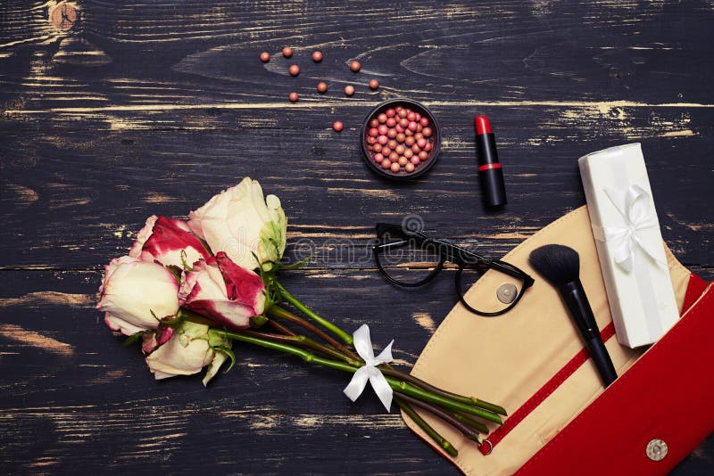 Sac rouge avec des cosmétiques, les verres et les roses sur le fond grunge photos stock Sac rouge avec des cosmétiques, les verres et les roses sur le fond grunge photos stock