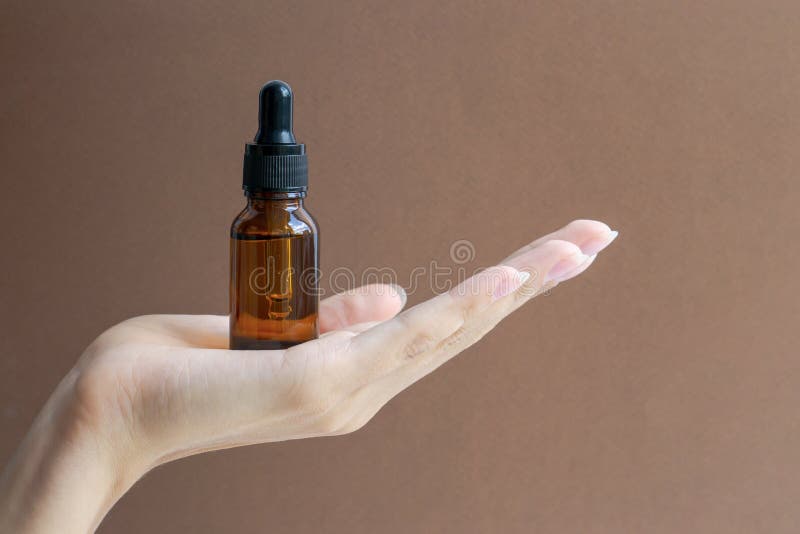 Saccheggio di bottiglie di vetro con contagocce sul palmo della mano delle donne. chiusura posizione di sfondo marrone per la copi immagini stock